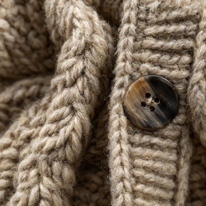 A close-up of cabled knit and a horn button.